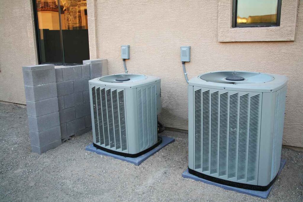 Two central air conditioning units next to each other outside of a residential space.