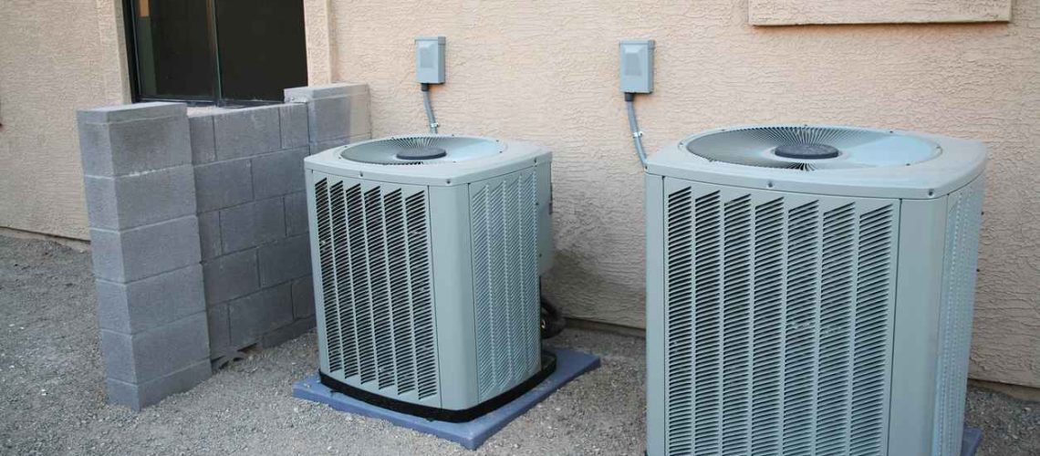 Two central air conditioning units next to each other outside of a residential space.