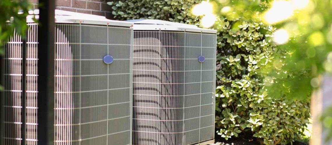Air conditioner unit outdoors in side yard of a brick home in hot summer season.